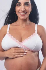 Soutien maternal sin aro, confeccionado en algodón elastizado blanco con detalles de puntilla rosada en el escote. Presenta un diseño cruzado para facilitar la lactancia, breteles elásticos regulables y cierre con broches en la espalda.