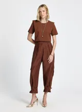 Remera de punto de algodón color terracota, de corte recto, largo estándar y mangas cortas. El diseño incluye superposiciones de tela en los hombros, creando un efecto estructurado y ligeramente geométrico. El cuello redondo presenta ribete acanalado y los laterales tienen pequeñas aberturas para un mejor ajuste.