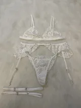 Conjunto de lencería compuesto por bralette de encaje con breteles regulables, tanga regulable y portaligas con volados en la cadera y ligas incorporadas.