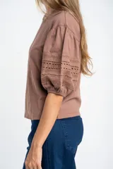 Remera negra de algodón con mangas cortas abullonadas que presentan detalles de encaje bordado y calado en los extremos.