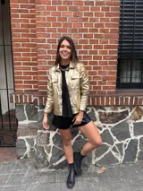 Chaqueta dorada metalizada con cuello camisero, cierre frontal con botones y bolsillos de parche en el pecho.