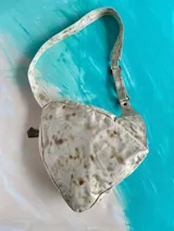 Mochila Kiri de cuero natural de la marca Carolina De Cunto, con diseño artístico pintado a mano de flores multicolores en el frente. Cuenta con una correa bandolera negra con el nombre de la marca en letras blancas y cierre superior con cremallera.