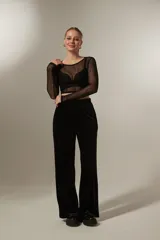 Pantalon de corte recto y tiro alto, confeccionado en tela de terciopelo negro con costuras verticales decorativas en el frente.