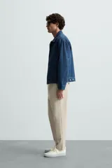 Pantalón chino de corte slim fit, confeccionado en tejido elástico. Presenta bolsillos frontales, bolsillos traseros de vivo con botón y cierre frontal con cremallera y botón.