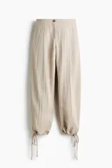 Pantalón tobillero de tiro alto en tejido arrugado color beige, con cierre de botón, bolsillos laterales y bajo ajustable con cordón.