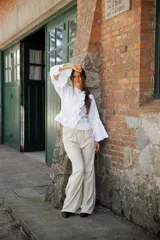 Pantalón de corte amplio y relajado, confeccionado en una mezcla de lino y algodón. Presenta un diseño de tiro alto con pinzas frontales que aportan estructura y una caída fluida.