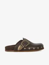 Zueco de cuero liso marrón con plantilla anatómica forrada en gamuza, hebilla ajustable estilo western en metal envejecido y tachas metálicas en el contorno.