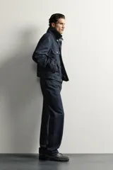 Campera de denim azul oscuro de corte cropped, con cuello camisero, bolsillos delanteros con solapa y cierre frontal oculto con botones metálicos.