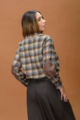 Camisa de manga larga con diseño a cuadros en tonos grises, marrones y ocres. Presenta cuello clásico, cierre frontal con botones, un bolsillo frontal y parches en los codos en contraste de color marrón.