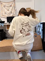 Buzo oversize color beige, con cuello redondo y diseño estampado en la espalda de temática cafetera con cafetera moka, taza, medialuna y sol.