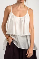 Top de tirantes blancos con diseño fluido y volado superpuesto en el pecho.
