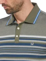 Polo de piqué color verde oliva con diseño jacquard. Presenta cuello clásico con borde celeste, tapeta de dos botones y mangas cortas con borde a tono. Tiene un bloque central con rayas horizontales en tonos verde, azul y blanco.
