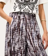 Pantalón aladín de cintura alta confeccionado en viscosa texturizada con estampado tie-dye en tonos oscuros. Presenta un corte amplio con volumen en las piernas y bajos afinados.