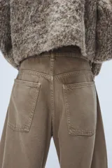 Jeans de tiro medio con diseño baggy barrel, confeccionados en denim color beige con efecto lavado. Presentan cinco bolsillos, costuras laterales torcidas y cierre frontal con cremallera y botón metálico.