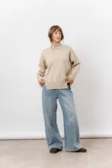 Sweater de tejido de punto color beige, con cuello alto, hombros caídos, mangas largas con puños acanalados y tajos laterales en el ruedo.