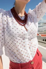 Camisa de estilo romántico confeccionada en tela broderie blanca, con mangas al codo abullonadas y cierre frontal con botones.