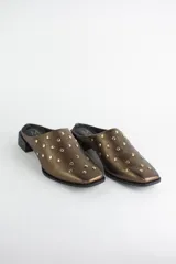 Zueco de cuero color bronce con punta almendrada y detalle de tachas metálicas doradas en toda la capellada. Posee un taco cuadrado bajo de 3 cm.