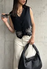 Chaleco negro de lino con bordado de palmeras en el ruedo, escote en V y cierre frontal con botones.