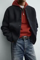 Chaqueta relaxed fit de color negro, confeccionada en tejido de canalé con mezcla de lana. Presenta cuello redondo, puños y dobladillo en rib elástico, bolsillos frontales de vivo y cierre con botones a presión.