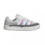 Zapatilla Adidas Adimatic de estilo skate, color gris claro con detalles en gris oscuro. Presenta tres franjas laterales en blanco, con ribetes finos en rojo y azul. La suela es gruesa y texturizada en la puntera.