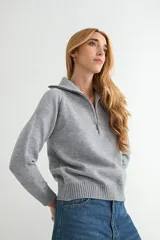 Buzo de punto gris con cuello polo y cierre frontal parcial, de manga larga y diseño holgado con puños y ruedo acanalados.