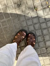 Sandalias de cuero marrón con tiras entretejidas y suela de goma negra.