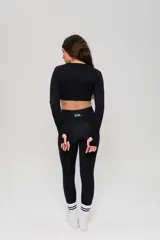 Conjunto deportivo de tres piezas en color negro, compuesto por un top de manga larga con cuello redondo y logo estampado, un top de bretel ancho y una calza chupín de tiro alto. El diseño presenta detalles de tejido con textura en zonas estratégicas.