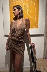 Vestido corto de gasa tornasol color cobre, con escote pronunciado en V, cuello halter y espalda baja. Presenta un diseño drapeado en la cadera con un lazo largo ajustable que permite múltiples usos.