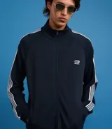 Campera deportiva de cuello alto con cierre frontal completo, mangas largas con rayas laterales blancas contrastantes y bolsillos laterales. Presenta un bordado pequeño en el pecho.