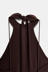 Vestido largo de color marrón oscuro con cuello halter y lazada en la nuca. Presenta un diseño con detalle de tejido drapeado efecto globo en la cintura y corte recto en la falda.