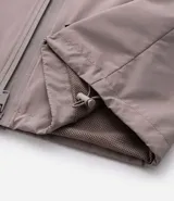 Campera rompevientos de color gris oscuro, con capucha ajustable mediante cordones, cierre frontal por cremallera y bolsillos laterales con cierre. Presenta puños elásticos y un diseño liso y minimalista.