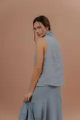 Chaleco de lino color marfil o beige claro, con diseño sin mangas, cuello alto amplio, cierre frontal con botones y bolsillos delanteros amplios. Presenta un corte asimétrico y relajado.