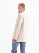 Blazer de tweed color beige, de corte recto y largo medio, con solapa clásica en contraste color blanco, dos bolsillos frontales con parche y cierre de dos botones plateados.