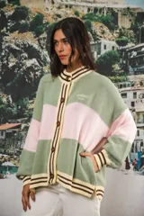 Cardigan de punto grueso oversized, con bloques de color verde menta y rosado. Presenta cuello redondo, puños y dobladillo con franjas amarillas y marrones. Cierre frontal con botones marrones y logo bordado en el pecho.
