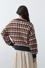Sweater de punto con diseño geométrico de rombos en tonos azul, marrón, beige y blanco. Presenta cuello redondo, puños y ruedo acanalados en color azul oscuro, con un calce relajado y mangas largas.