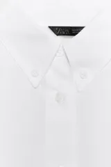 Camisa blanca de manga larga, confeccionada en popelín de algodón 100%. Presenta cuello solapa, cierre frontal de botones y un bolsillo de plastrón en el delantero.