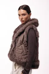 Chaleco acolchado color marrón con terminaciones de piel sintética en los bordes y cuello, aportando volumen y textura.