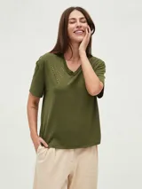 Remera blanca de manga corta con cuello en V y apliques de tachas metálicas doradas dispuestas en forma de V invertida en la zona de los hombros.