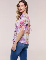 Blusa de gasa liviana con estampado floral en tonos violeta y rosado, cuello redondo y mangas cortas con detalle de lazo en los puños.