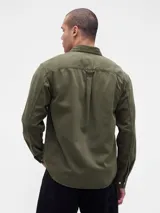 Camisa de jean de corte clásico en color azul oscuro, con cierre frontal de botones, cuello camisero y dos bolsillos frontales con solapa y botón.