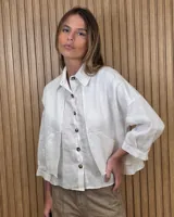 Sobrecamisa de lino color blanco, de corte amplio y mangas largas, con bolsillos laterales y cierre frontal de botones oscuros.