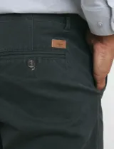 Pantalón de vestir verde oliva, de corte slim fit, sin pinzas, con bolsillos laterales y traseros. Se ajusta a la cintura con cinturón de cuero marrón.