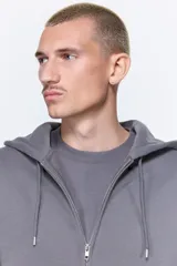 Campera con capucha de felpa gris oscuro, con interior cepillado suave. Modelo de hombros caídos, cierre frontal, bolsillos canguro delanteros y puños y bajo en punto acanalado.