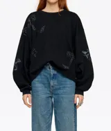 Sudadera negra de corte holgado y manga larga abullonada, con cuello redondo. Presenta detalles de pedrería brillante y estampados sutiles distribuidos por la prenda.