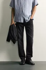 Jeans regular fit de mezclilla negra con efecto lavado, corte recto y tiro medio. Cuenta con diseño de cinco bolsillos y cierre frontal con cremallera y botón.