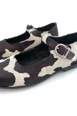 Zapato Mary Jane con estampado de vaca en blanco y negro, con correa al tobillo y hebilla plateada.