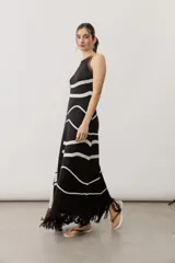 Vestido largo de punto con diseño geométrico y de ondas en color negro y crudo, sin mangas, con escote halter y detalle de flecos en el ruedo.