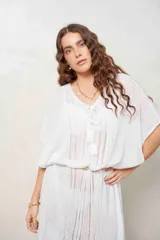 Poncho de hilo tejido en color blanco, con diseño translúcido, escote en V con cordones y borlas colgantes, y mangas murciélago amplias.