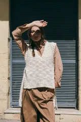 Chaleco tejido de lana rústica en color crudo, con cuello en V y aberturas laterales ajustables con lazos.