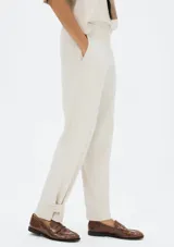 Pantalón de lino color beige, de corte recto y tiro medio, con detalle de pequeña abertura y botón en el dobladillo inferior.